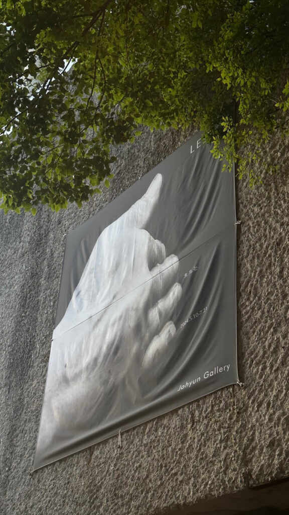 Exhibition poster banner displayed on the rough chiseled stone exterior wall of Johyun Gallery Busan