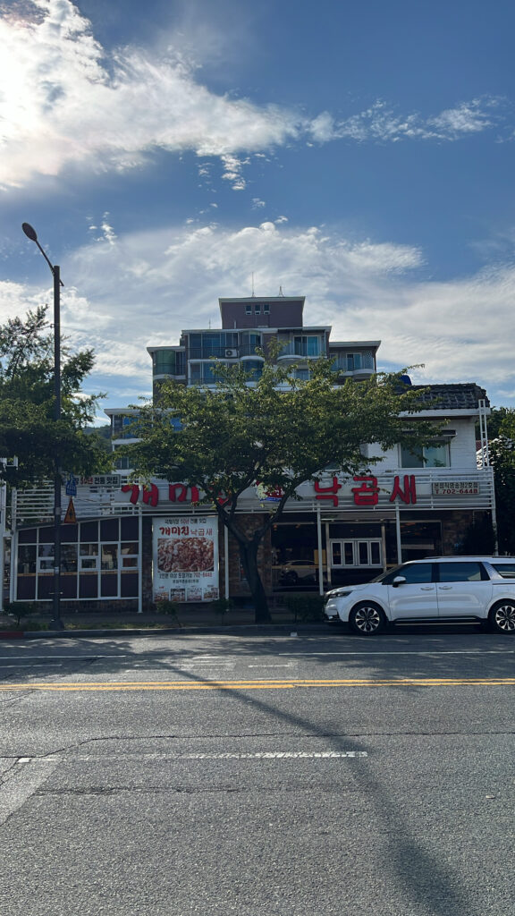Exterior view of Gaemijip Songjeong restaurant and the surrounding street under a clear sky.