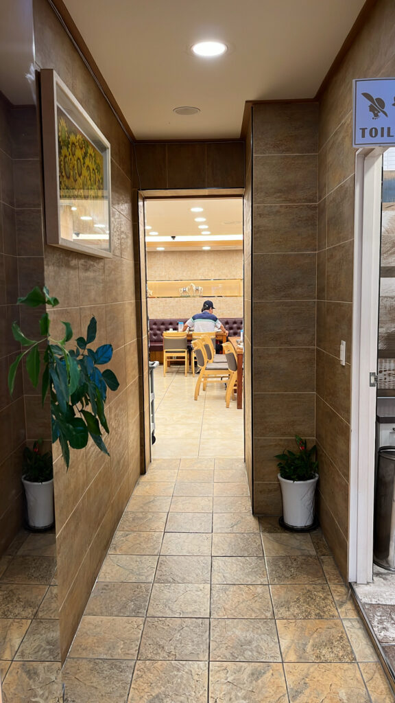 A clean hallway inside the restaurant with potted plants and a sunflower painting on the wall.