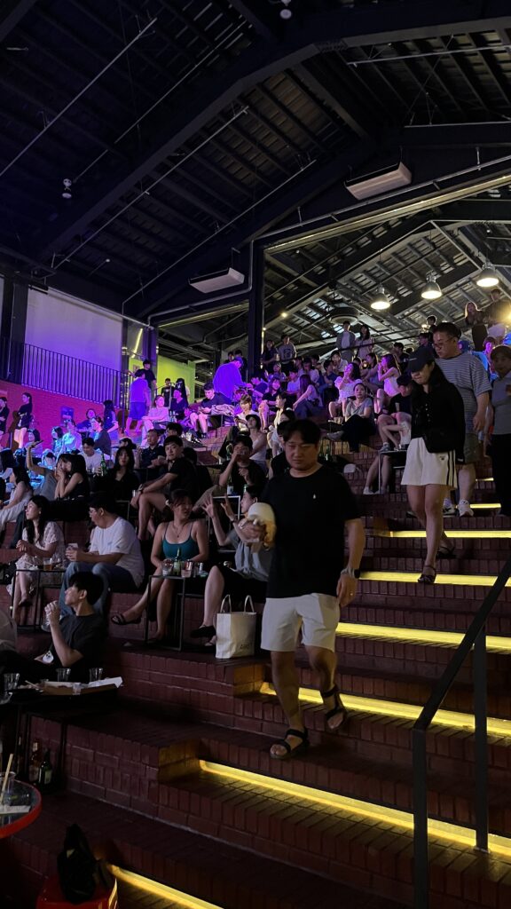 Multi-tiered brick stair seating filled with people enjoying drinks at Millac The Market at Night