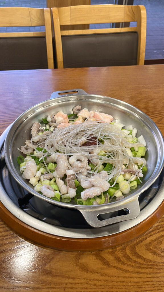 Close-up of raw ingredients in a pot including octopus, beef intestines, shrimp, chopped green onions, and glass noodles.