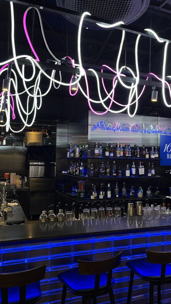 Stylish cocktail bar with blue neon lighting and liquor bottles at Millac The Market at Night
