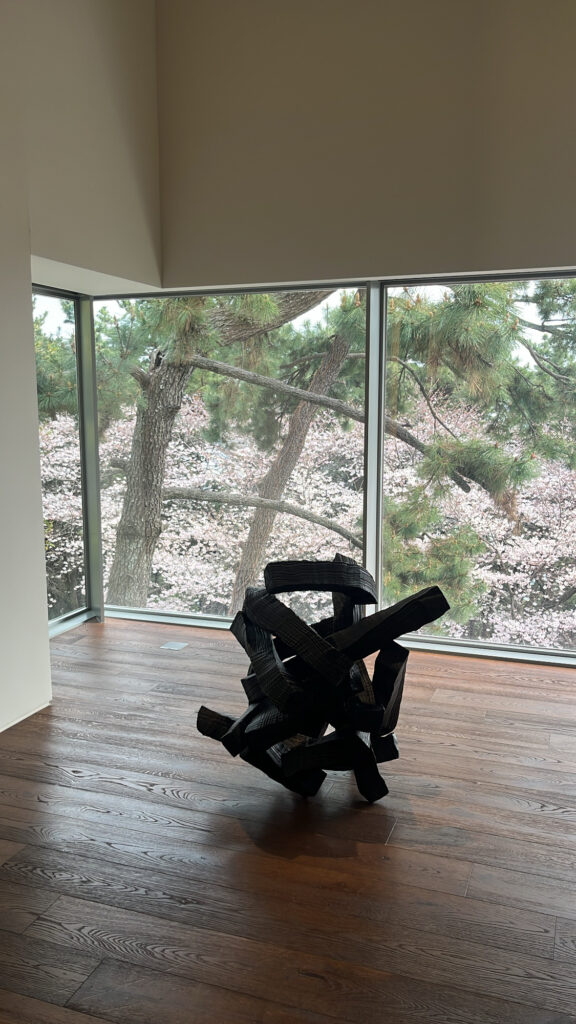 Lee Bae sculpture against large window with cherry blossom view at Johyun Gallery Busan