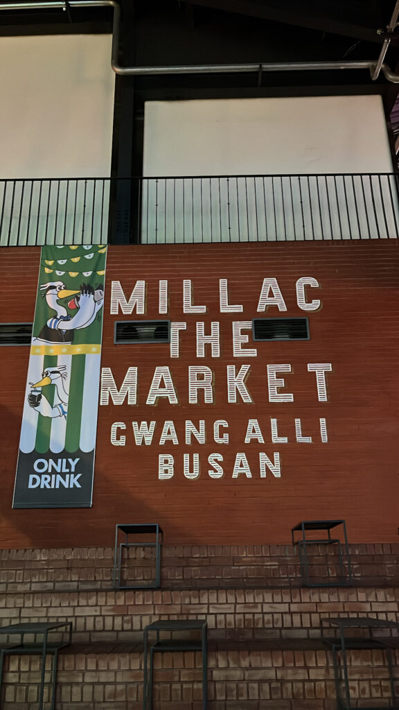Large brick wall with Millac The Market logo and seagull mascot illustration in Busan