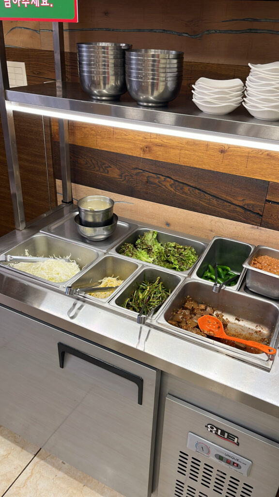 A self-service side dish bar with fresh cabbage salad, chives, bean sprouts, and acorn jelly.