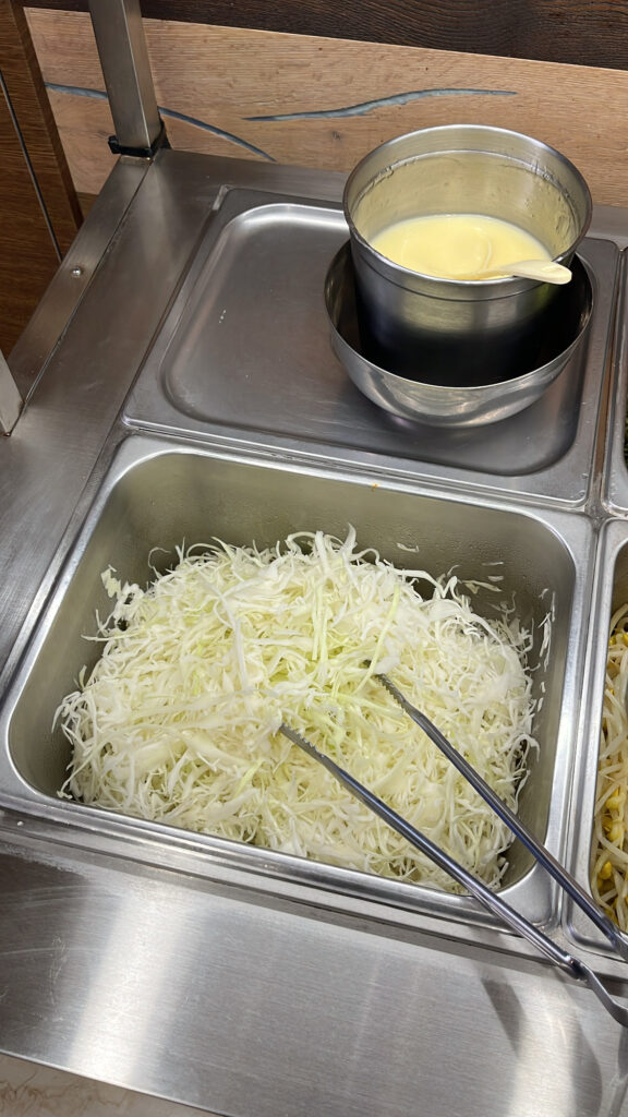 A stainless steel container filled with shredded fresh cabbage and salad dressing at the self-bar.