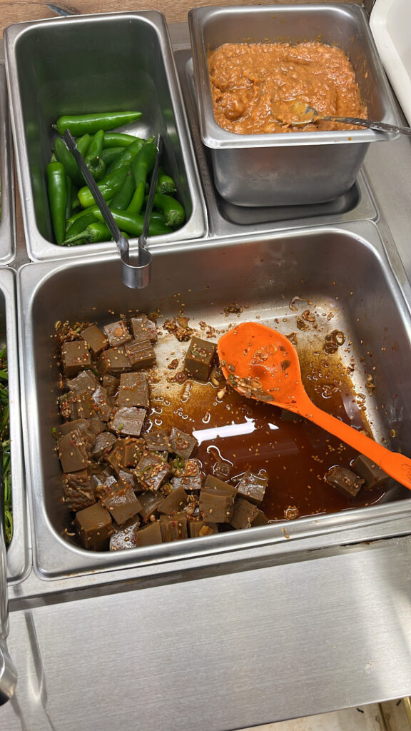 Seasoned acorn jelly cubes, green chili peppers, and ssamjang at the self-service bar.