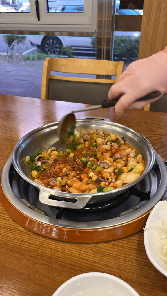 A staff member stirring the boiling octopus, beef intestines, and shrimp stir-fry with a ladle.