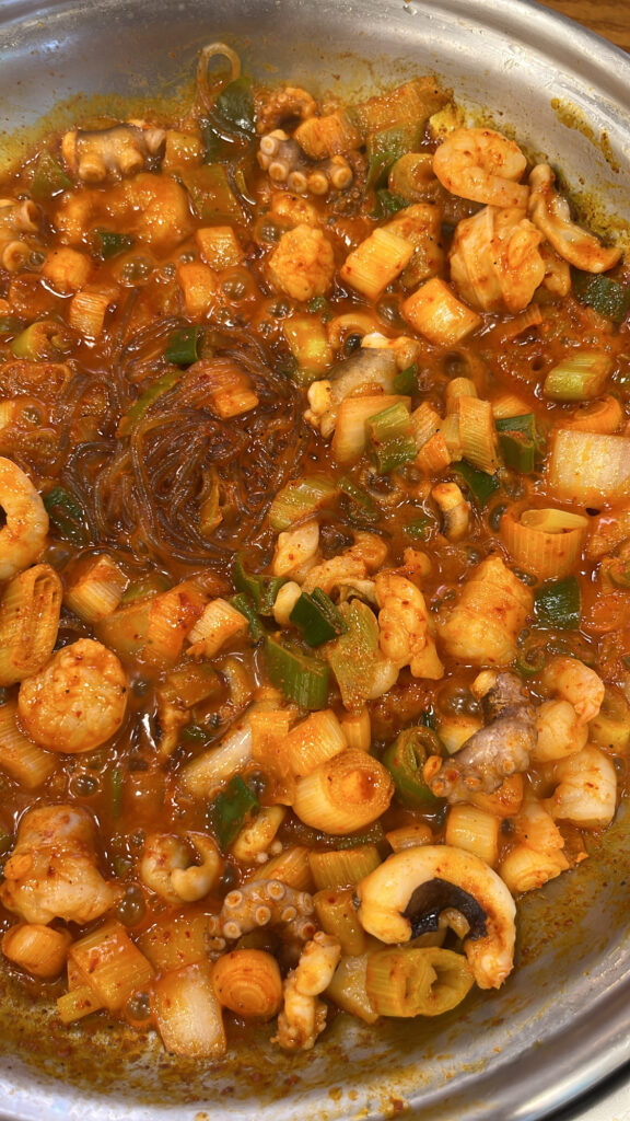 A close-up shot of cooked spicy Nakgopsae with octopus, intestines, shrimp, and glass noodles.