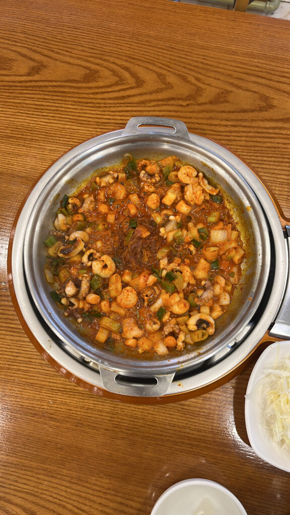 A top-down shot of fully cooked spicy Nakgopsae with octopus, intestines, shrimp, and glass noodles in a metal pot.