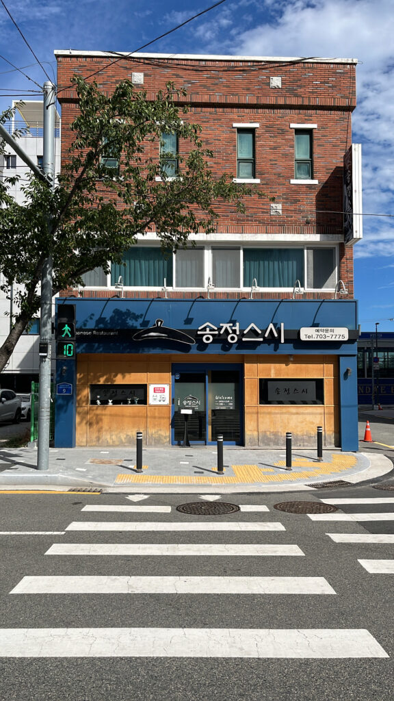 Exterior building and storefront view of Songjeong Sushi Busan located along the main road