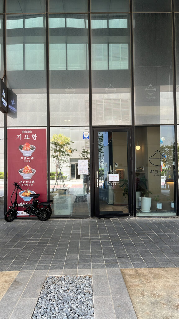 Glass storefront entrance of Giyohang Haeundae with poster signboards on the pillar