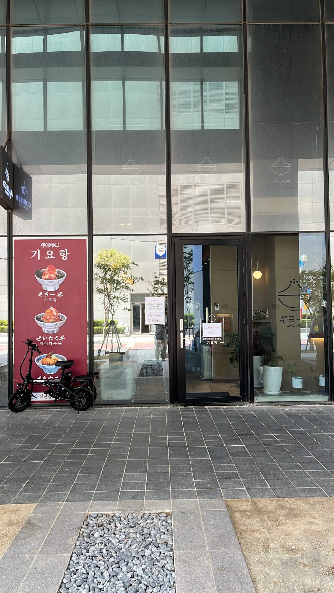 Glass storefront entrance of Giyohang Haeundae with poster signboards on the pillar