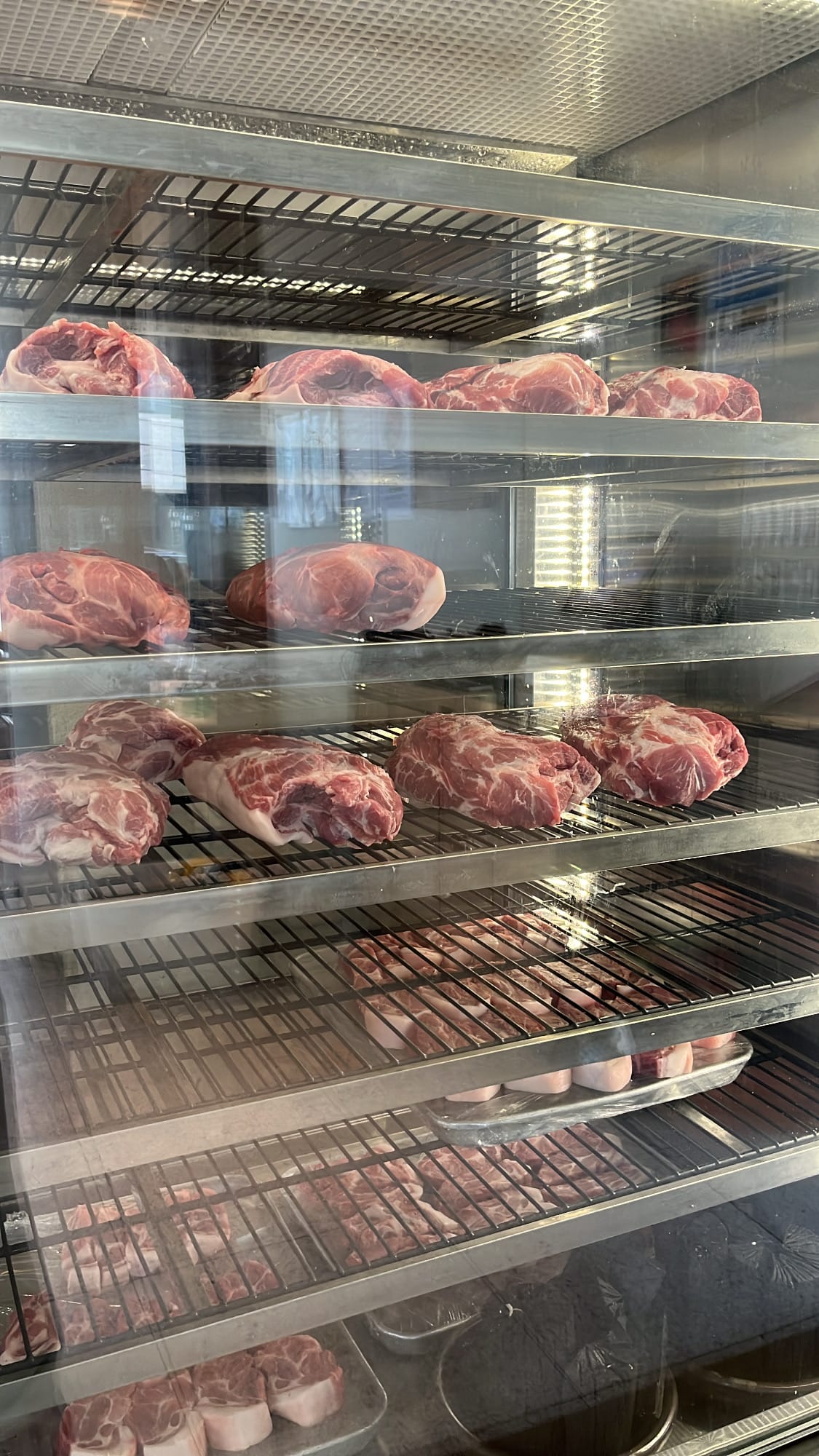 Close-up of carefully aged prime pork cuts resting inside the glass meat refrigerator