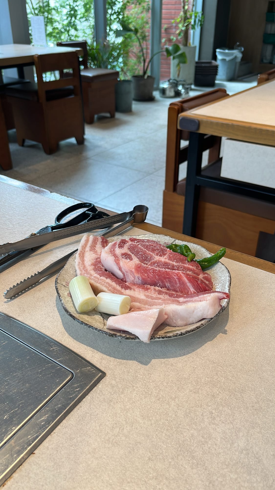 เนื้อหมูดิบที่ผ่านการบ่มไว้อย่างดี หั่นชิ้นหนาและสดใหม่ ถูกจัดวางบนจานข้างเตาย่างบนโต๊ะที่ร้าน Gohasoon