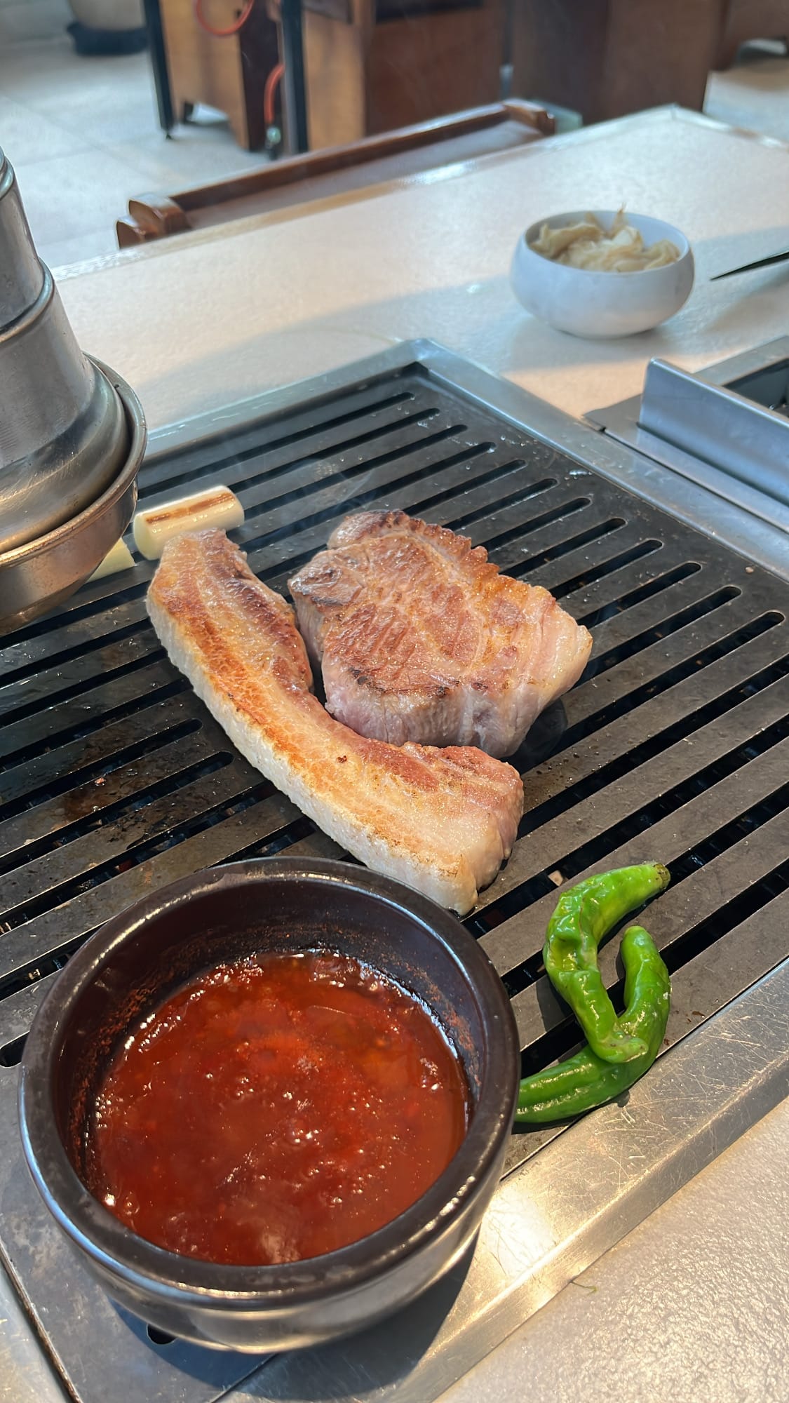 Thick pork meat sizzling on the charcoal grill grate at Gohasoon Gwangalli