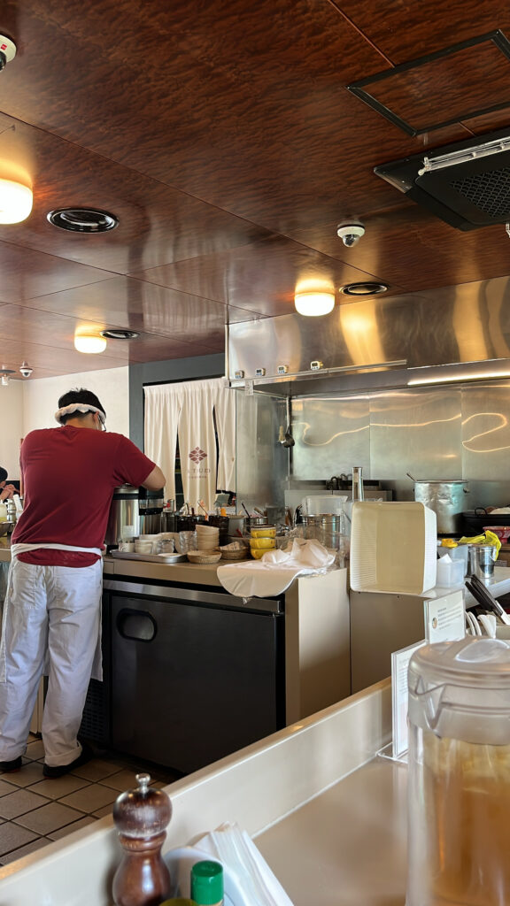 Chef cooking fresh ramen in the open kitchen behind the counter at Matsudo Busan