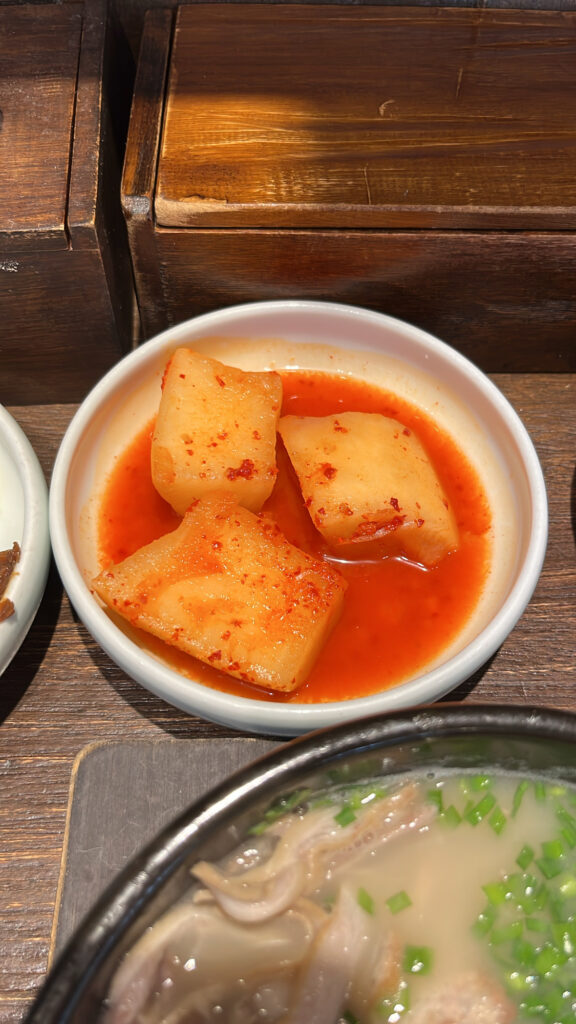 Spicy cubed radish kimchi (Kkakdugi) next to pork soup bowl