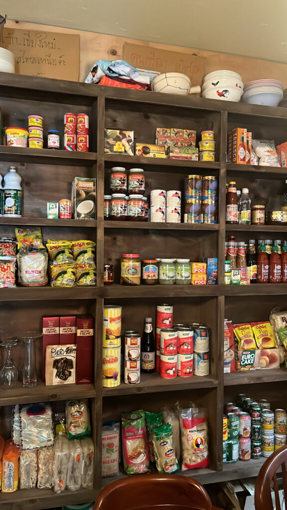 Wooden shelves filled with imported Thai sauces, spices, and groceries at Pili Pili