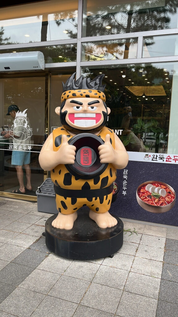Wandduk Sundubu mascot character standing outside the 24-hour Busan restaurant