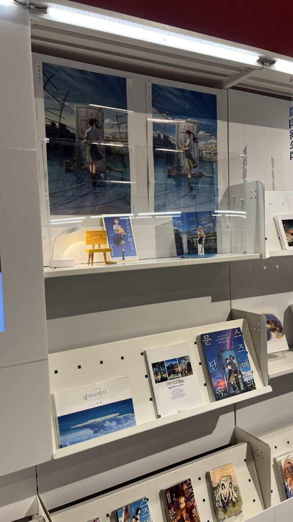 Curated exhibition stand displaying books and media related to "Suzume" animation