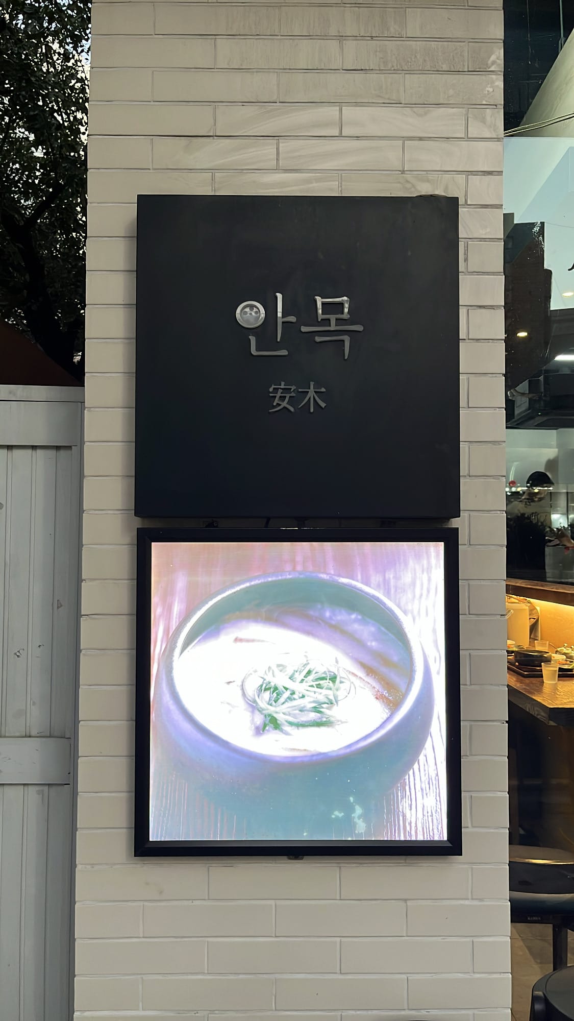 Sleek black exterior signboard and illuminated pork soup display at Anmok Busan