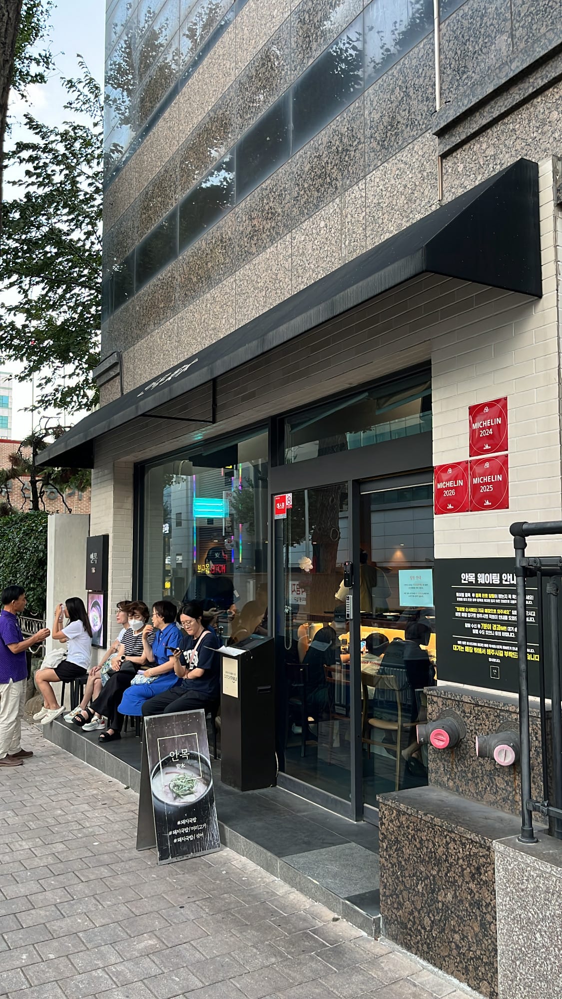 Restaurant entrance of Anmok Busan displaying three Michelin Guide plaques and waiting guests