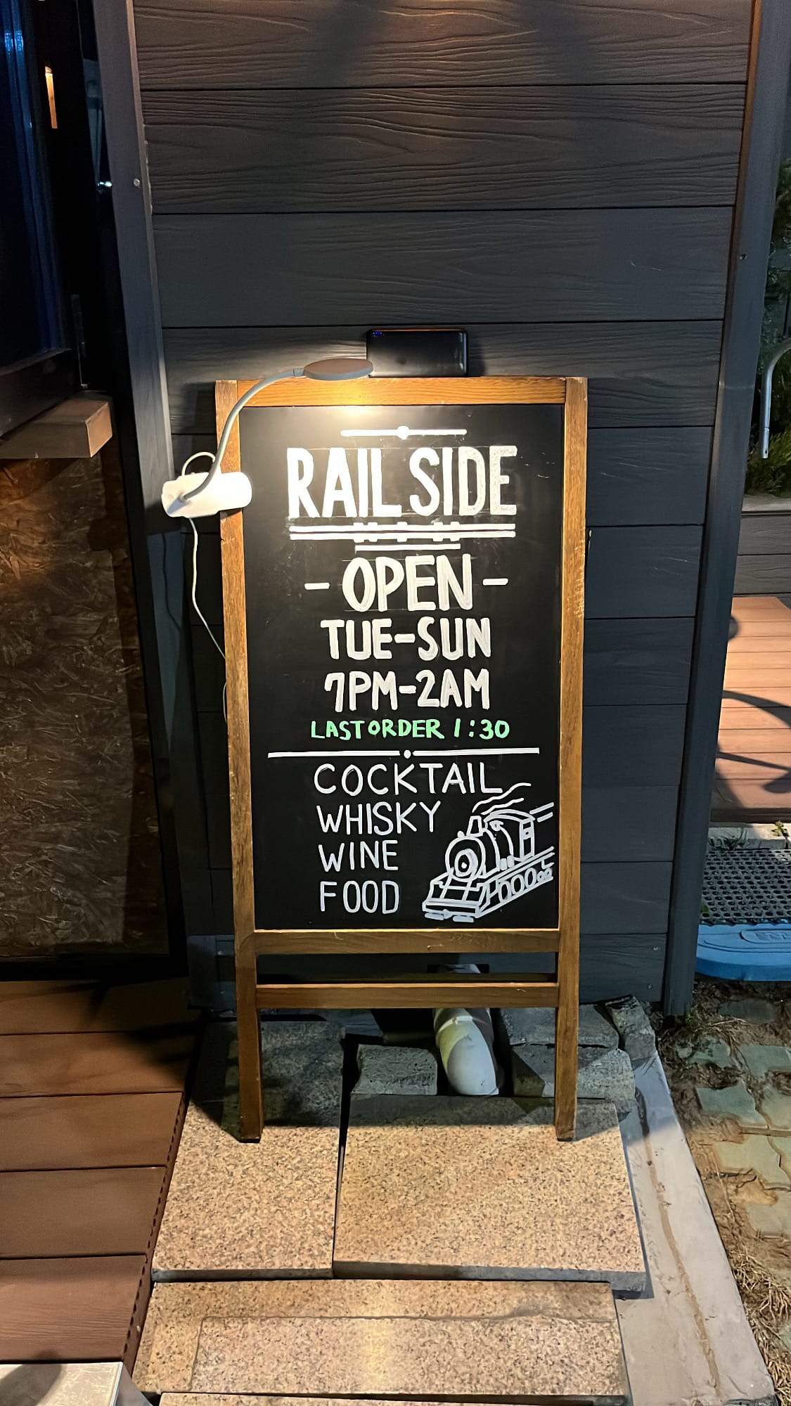 Wooden chalkboard menu sign displaying operating hours at Bar Railside