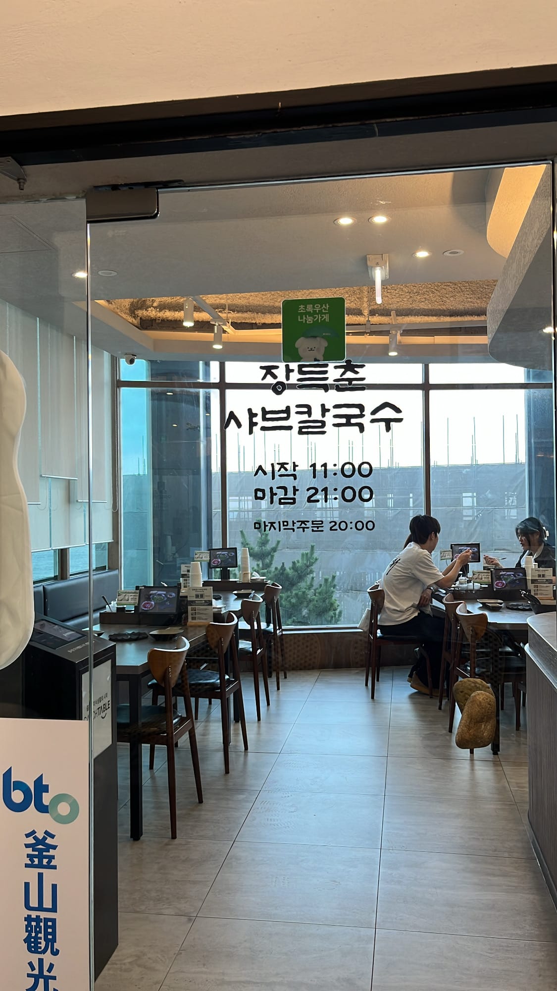 Glass entrance door showing business hours at Jang Deuk Chun Shabu Kalguksu