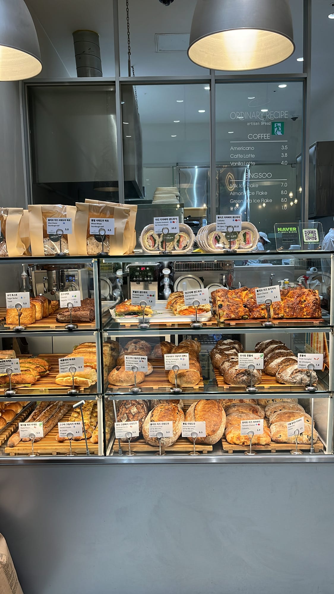 Multi-tier glass showcase loaded with sourdough loaves, baguettes, and focaccia at Ordinary Recipe Centum