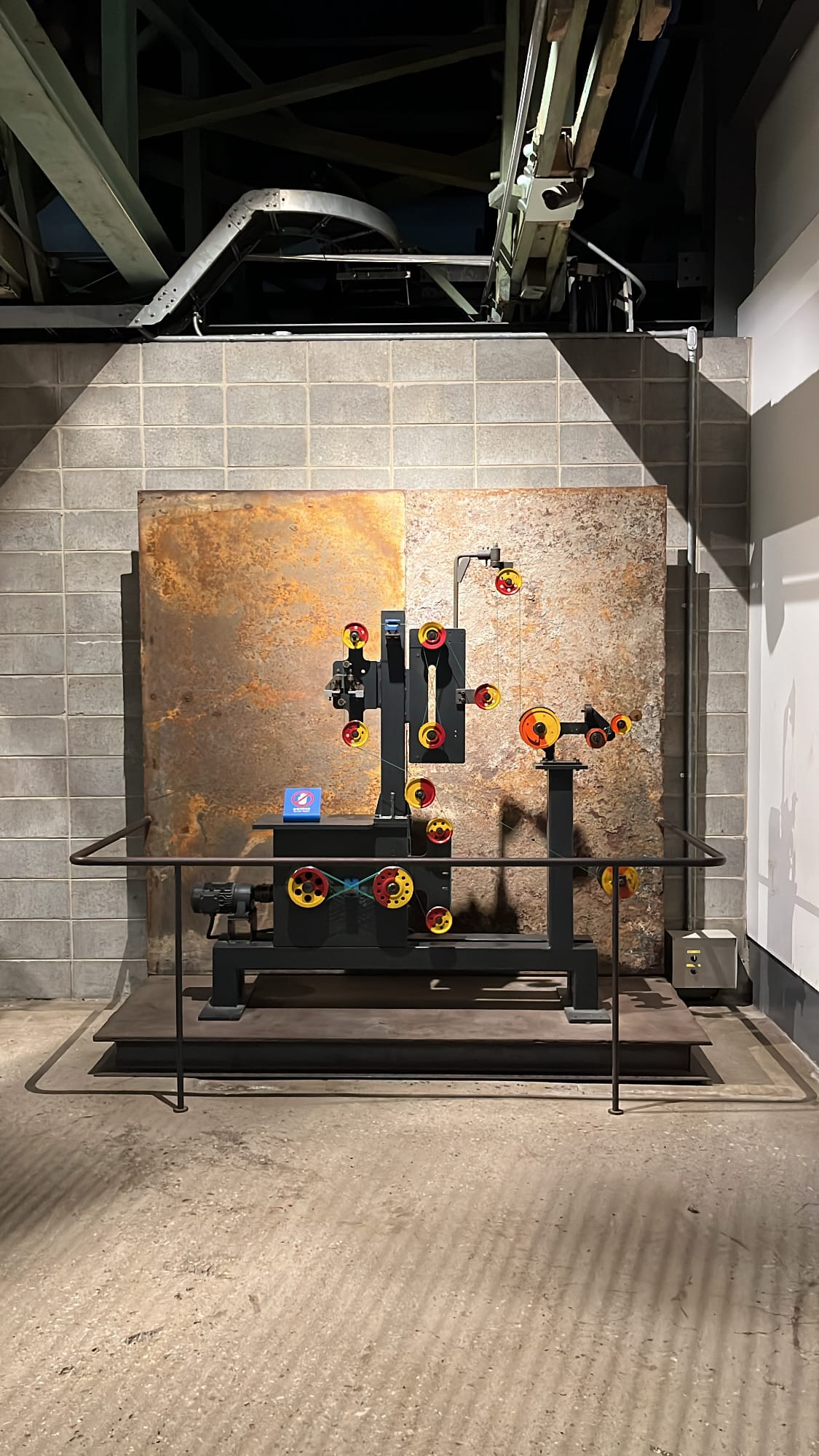 Historic wire factory machinery preserved against rusted steel wall