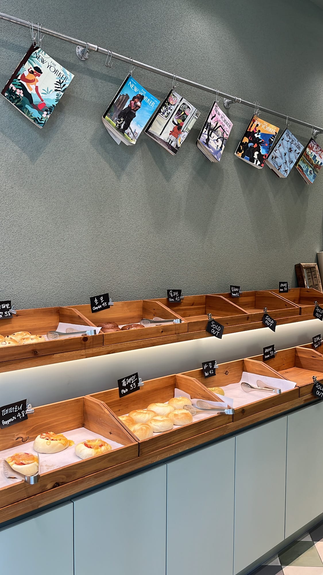 Wooden bakery shelves lined with fresh bagels along the wall at Bagel Then You Busan Centum