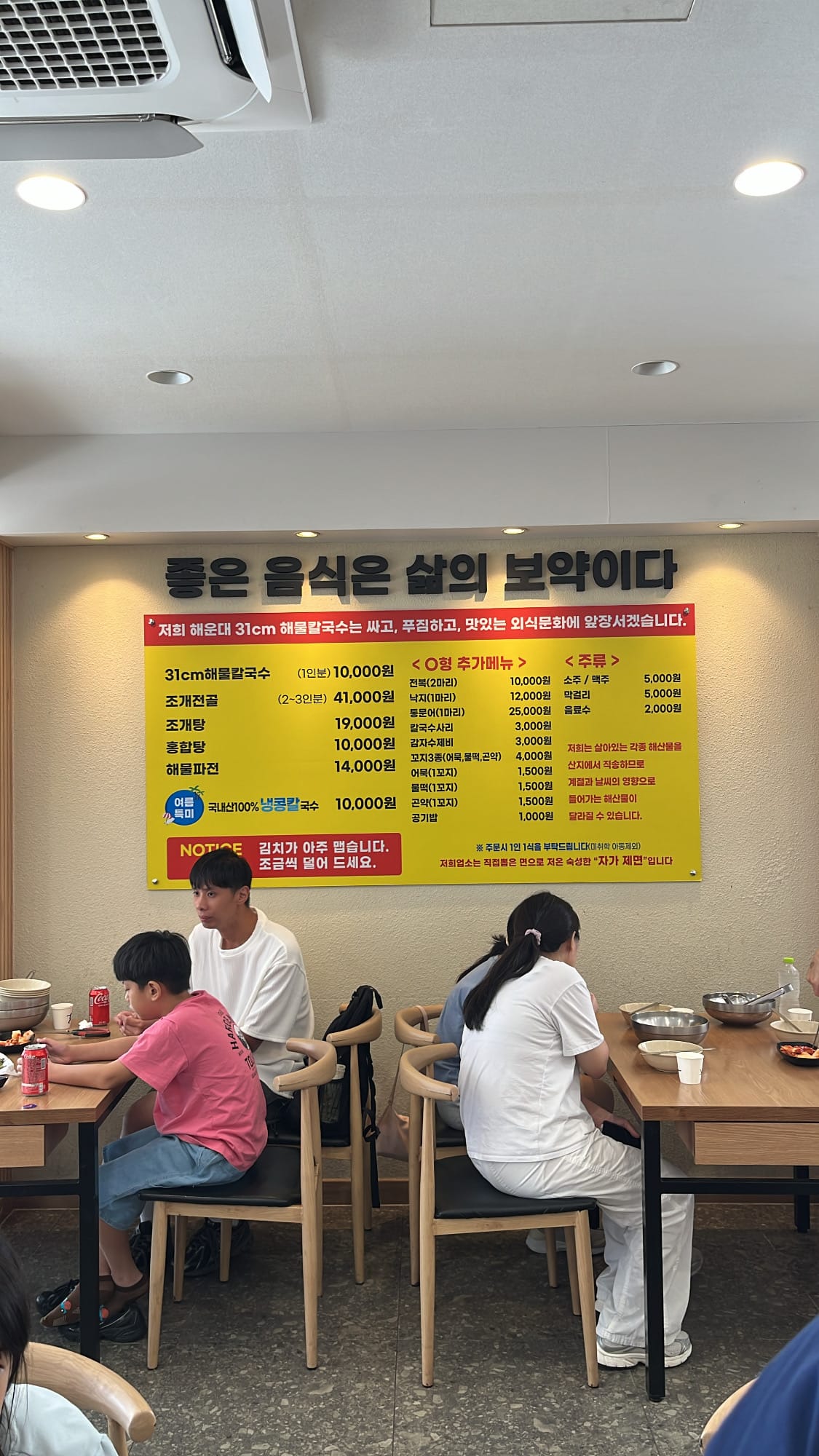 Bright yellow wall menu board inside Haeundae 31cm Seafood Kalguksu restaurant