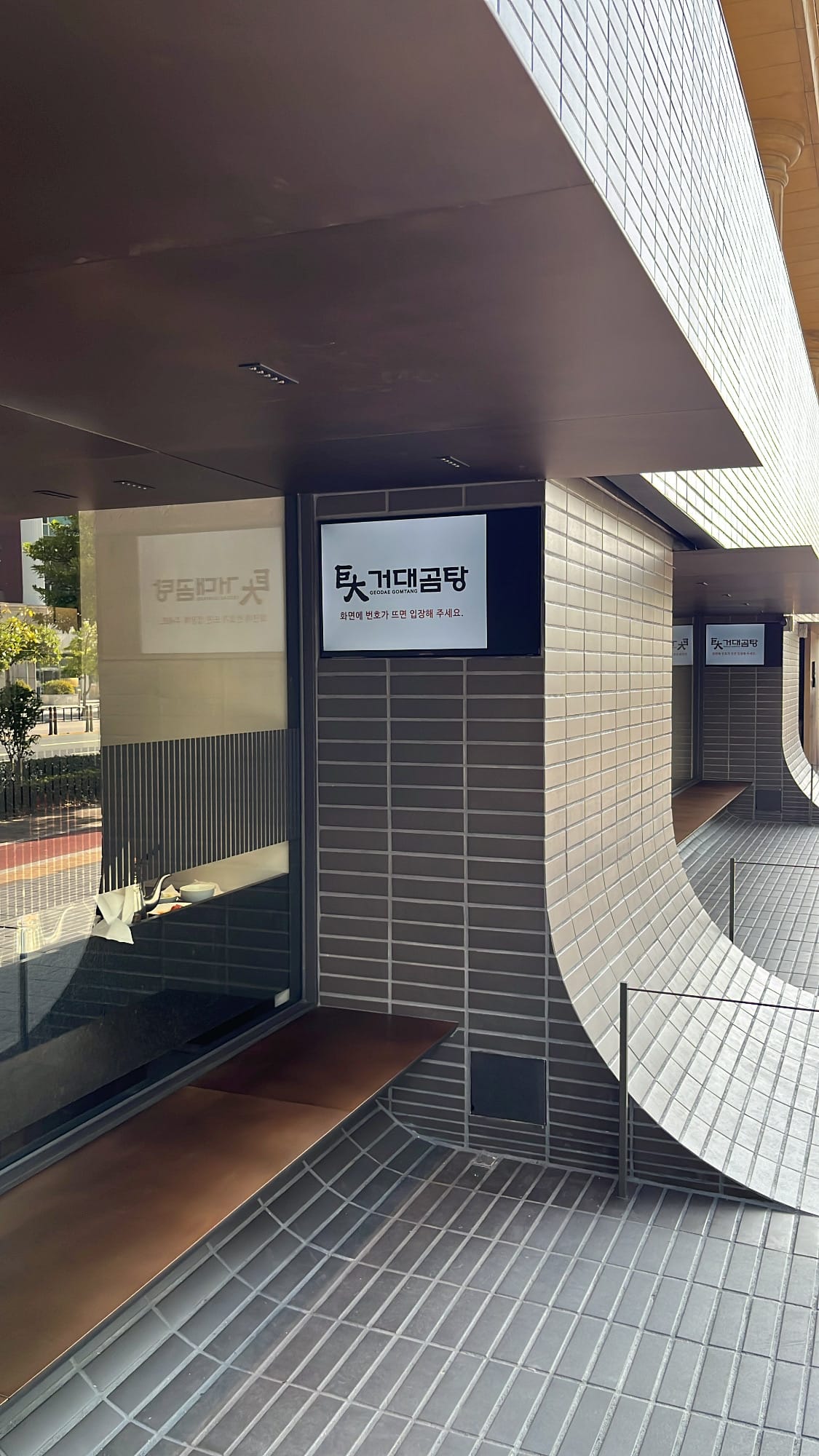Outdoor waiting seating area with TV screen calling queue numbers at Geodae Gomtang Busan