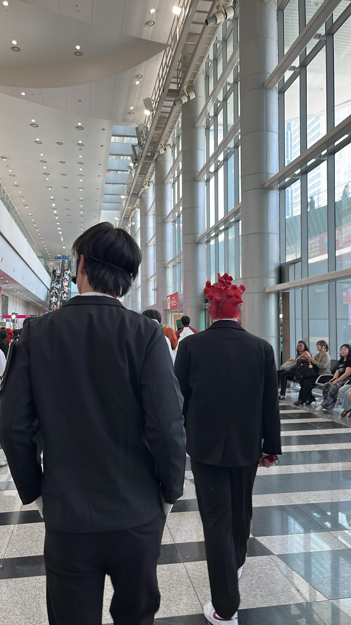 Cosplayers in tailored black suits walking through BEXCO concourse