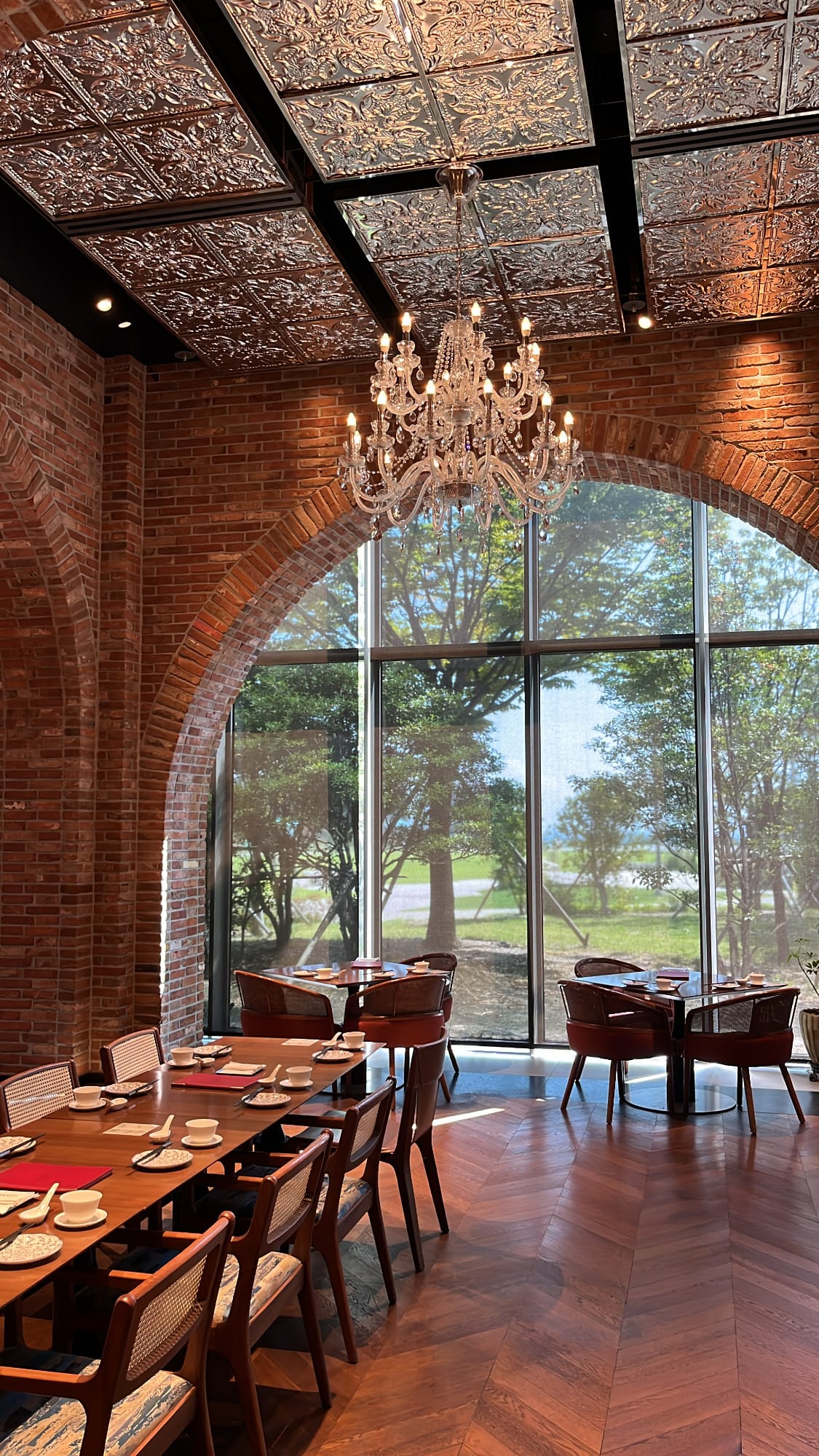 Sunny dining tables overlooking green garden scenery under brick arches at Village de Ananti Lou Busan