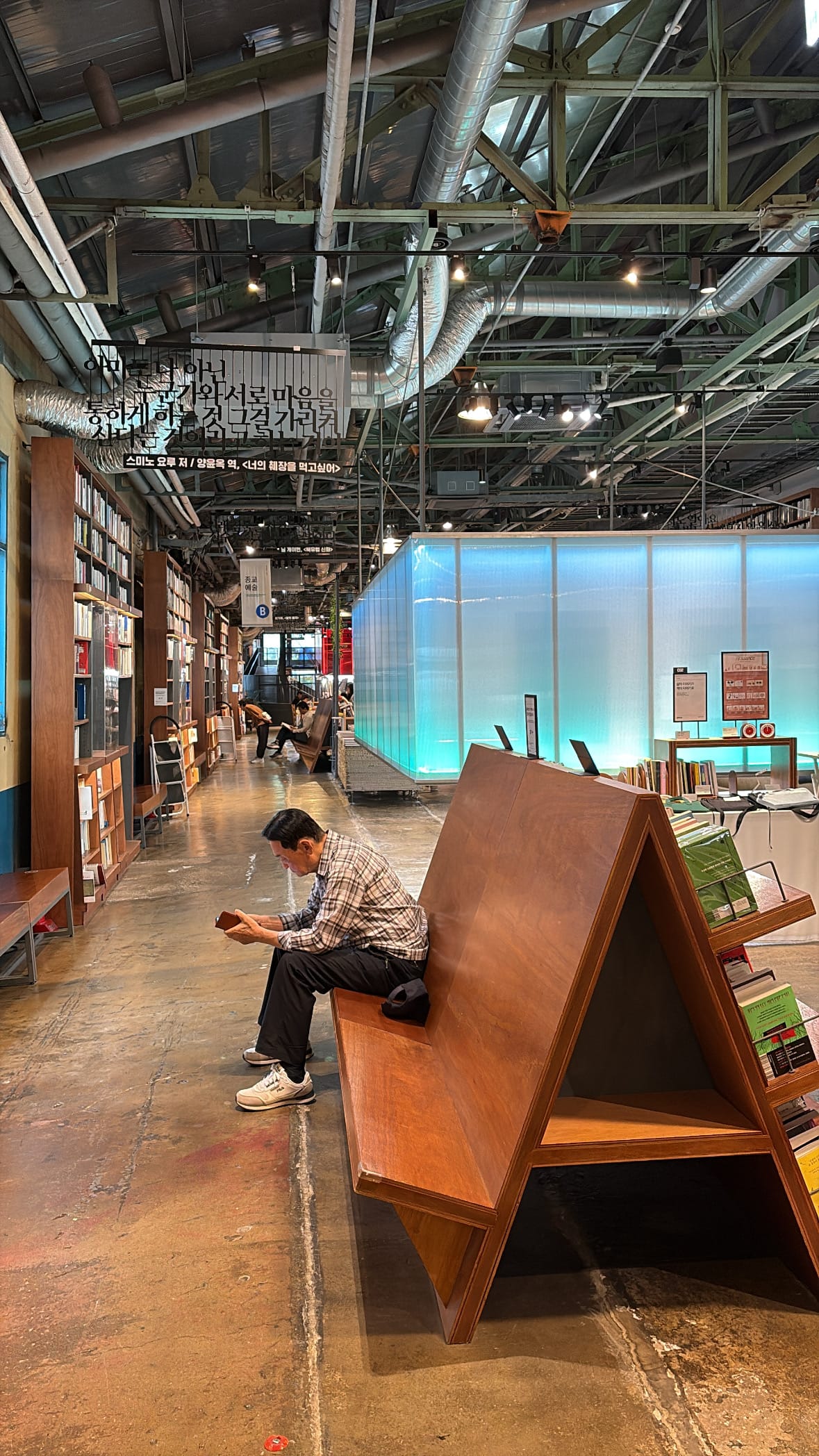 Visitor reading peacefully on a wooden triangular bench at YES24 Busan