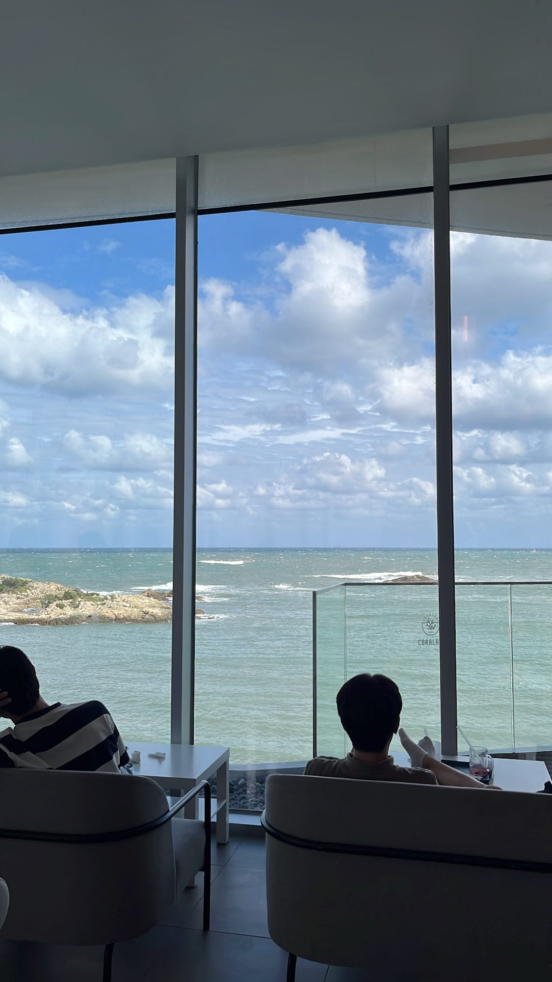 Floor-to-ceiling glass windows at Coralani Busan framing coastal waves and blue skies