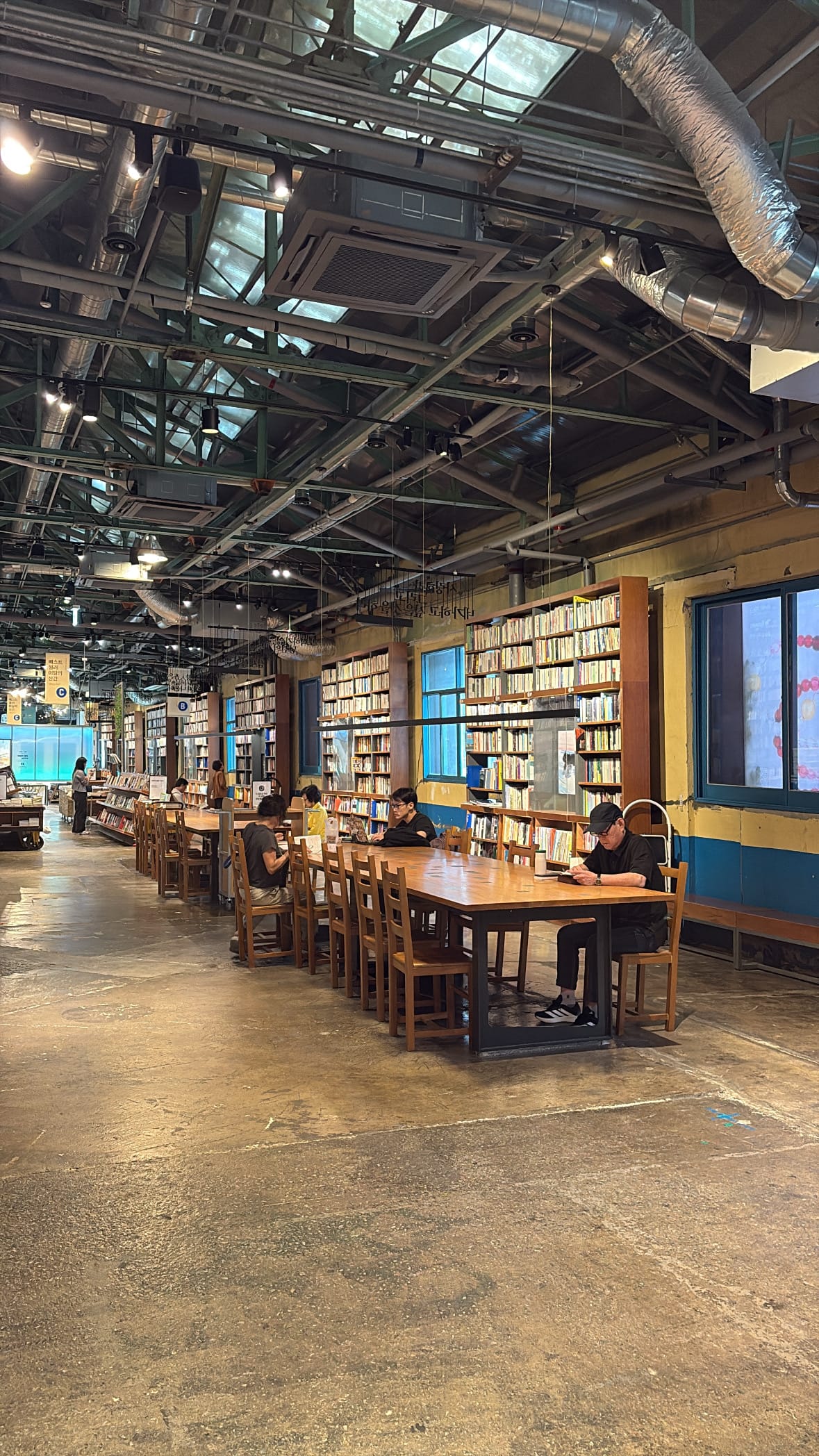 Guests studying and reading at a large communal wooden table in YES24 Busan