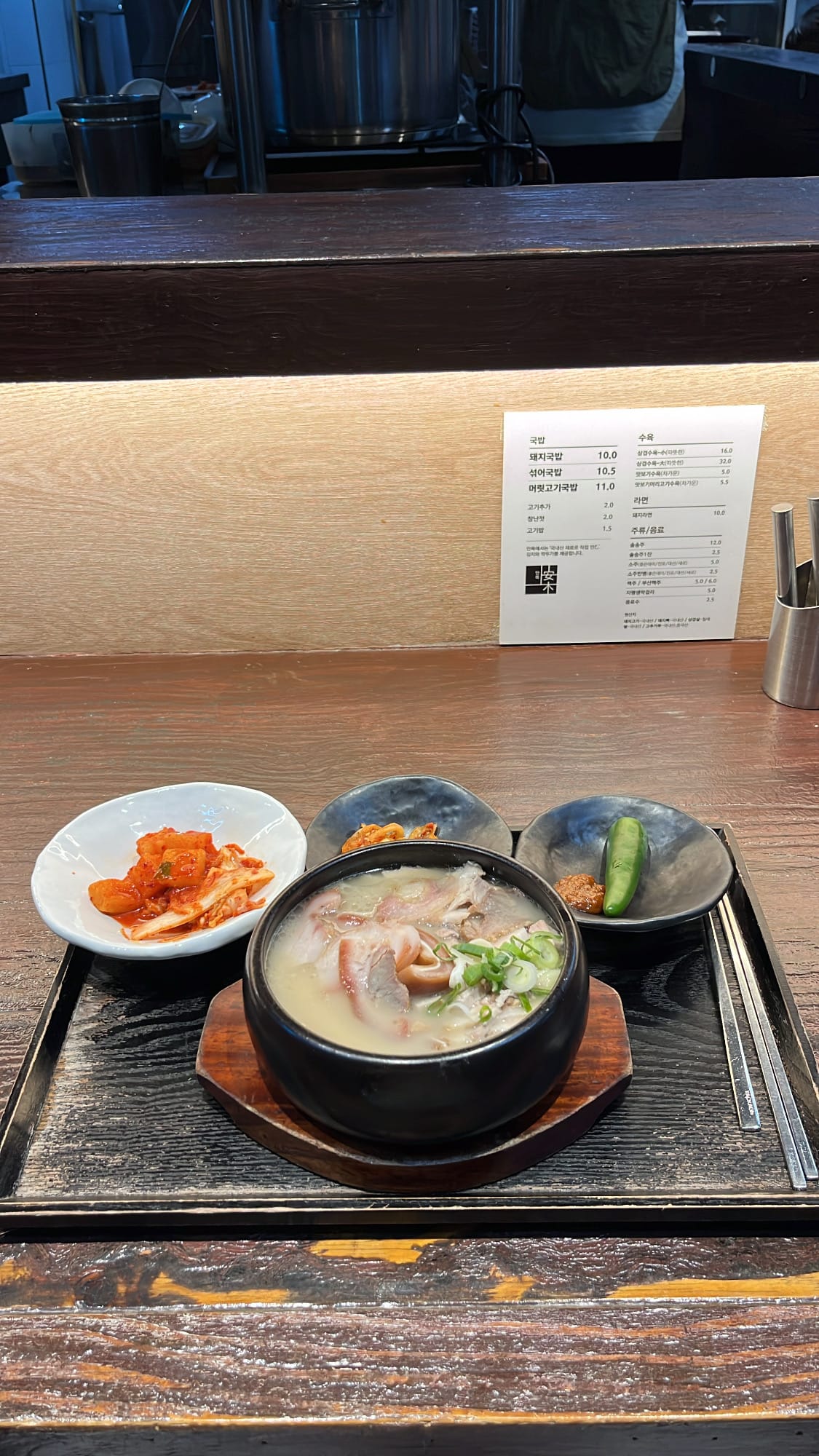 Full wooden tray setting with mixed dwaeji gukbap, extra pork meat, and side dishes at Anmok Busan