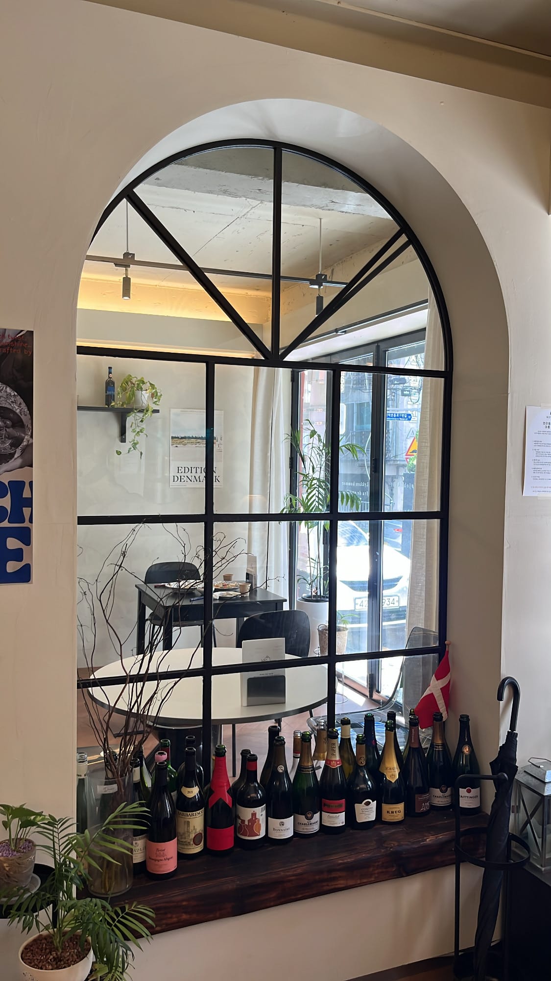 Danicci curated wine bottles lined up beneath large arched window