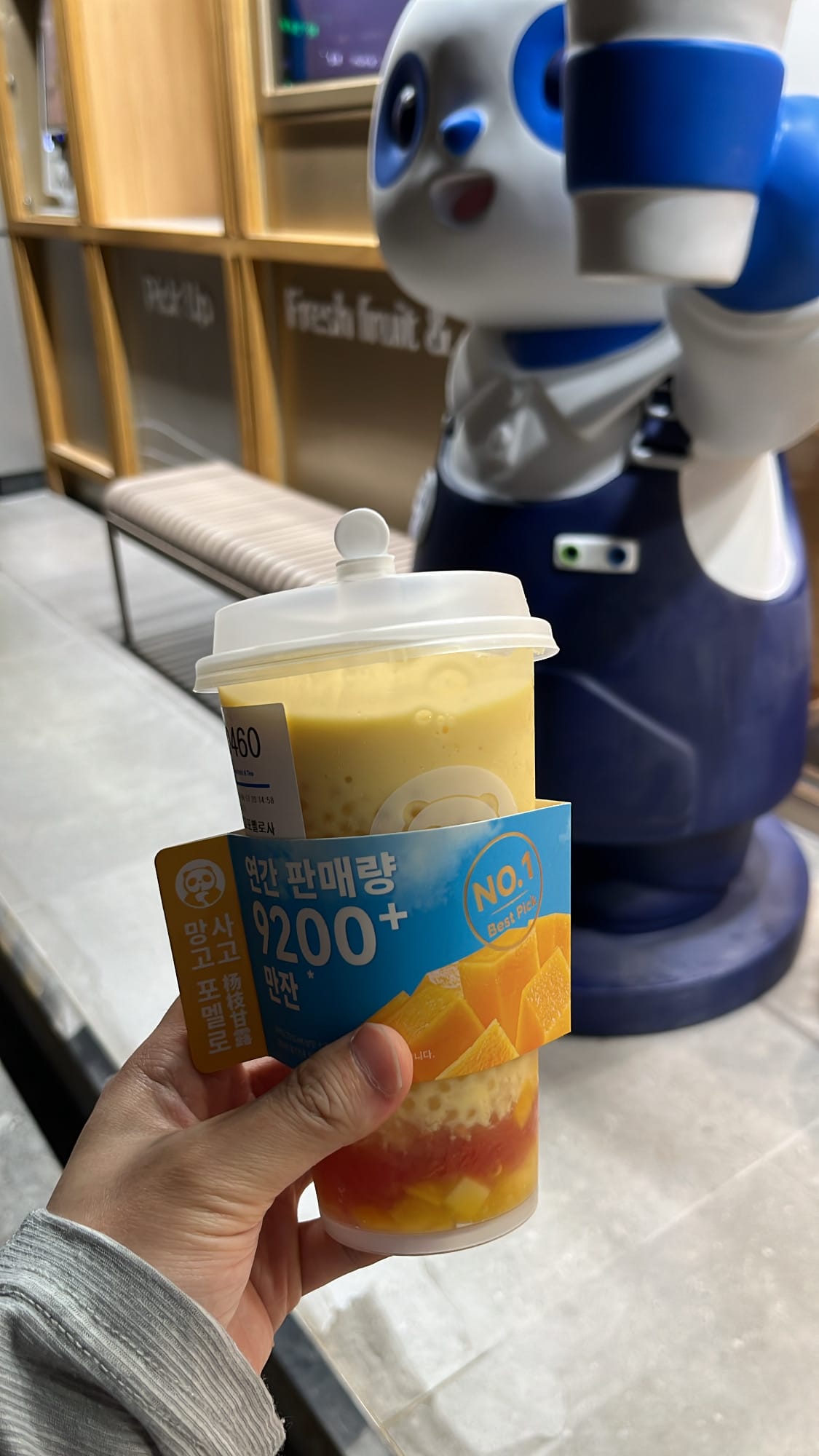 Mango Pomelo Sago cup with blue sleeve held in front of panda mascot at ChaPanda Busan Centum