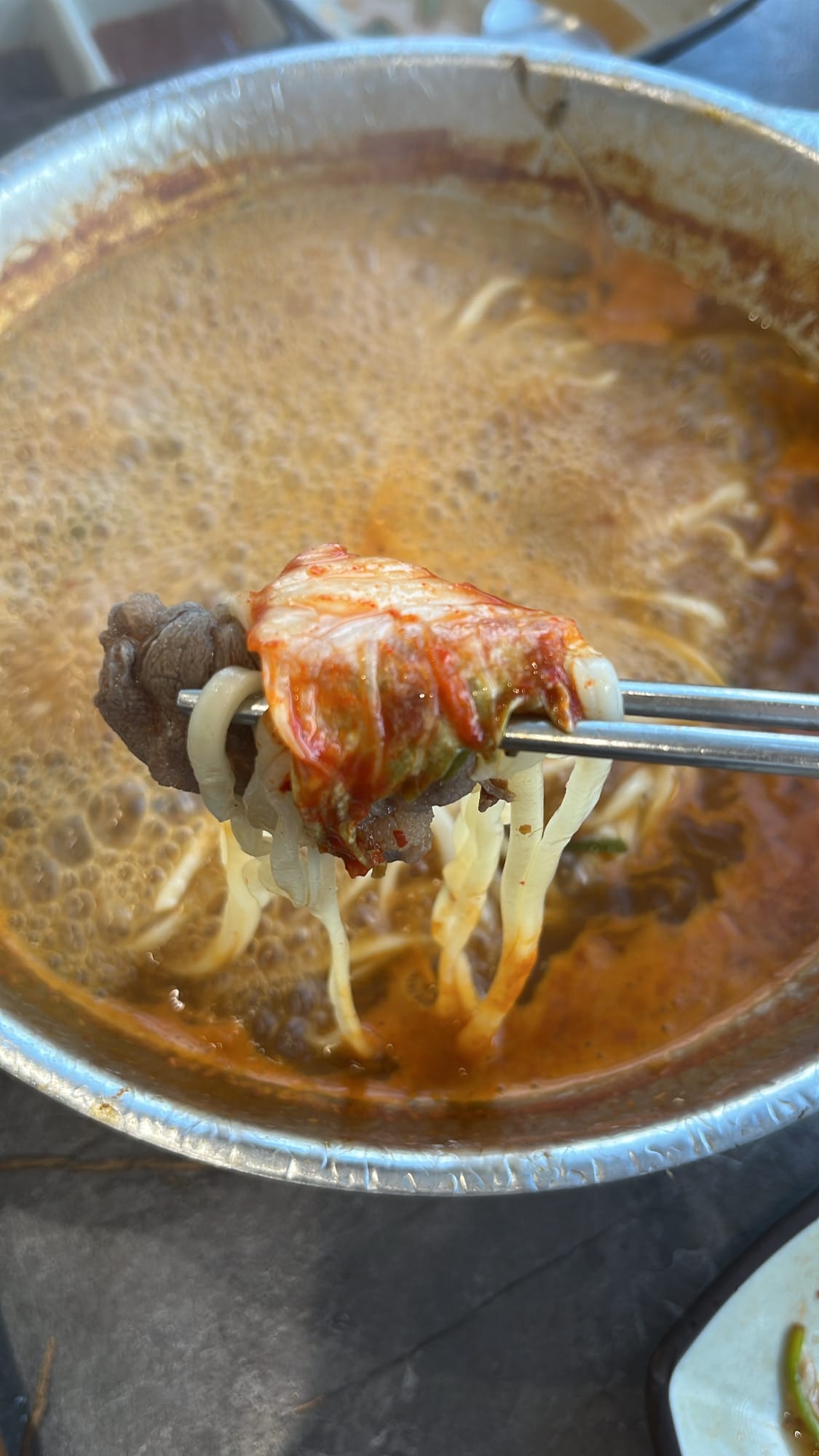 Lifting cooked handmade kalguksu noodles topped with fresh kimchi using chopsticks