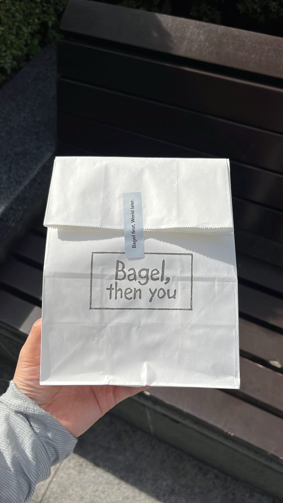 White paper takeaway bag stamped with logo held outside Bagel Then You Busan Centum