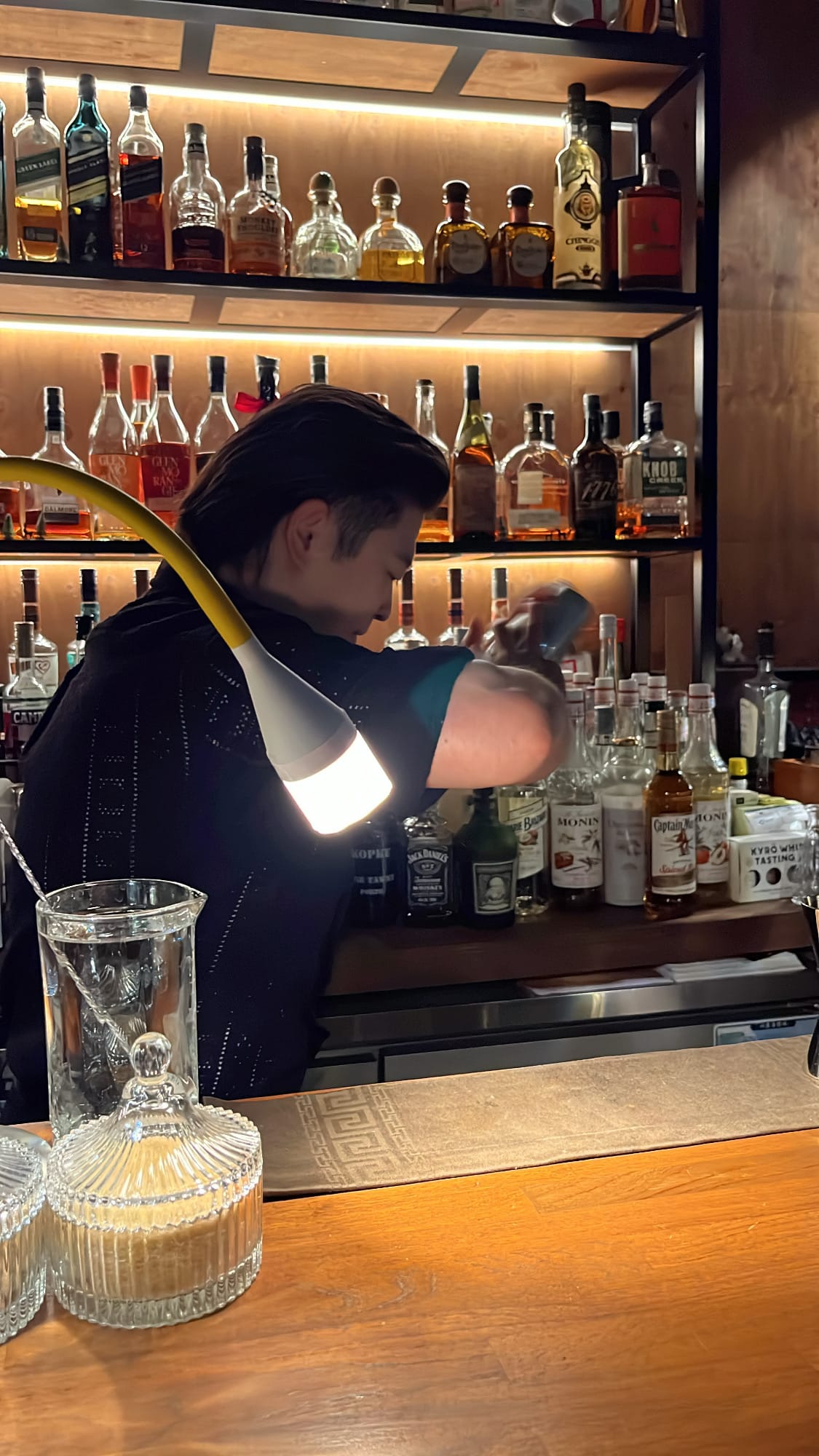 Bartender vigorously shaking cocktail shaker in front of illuminated bar