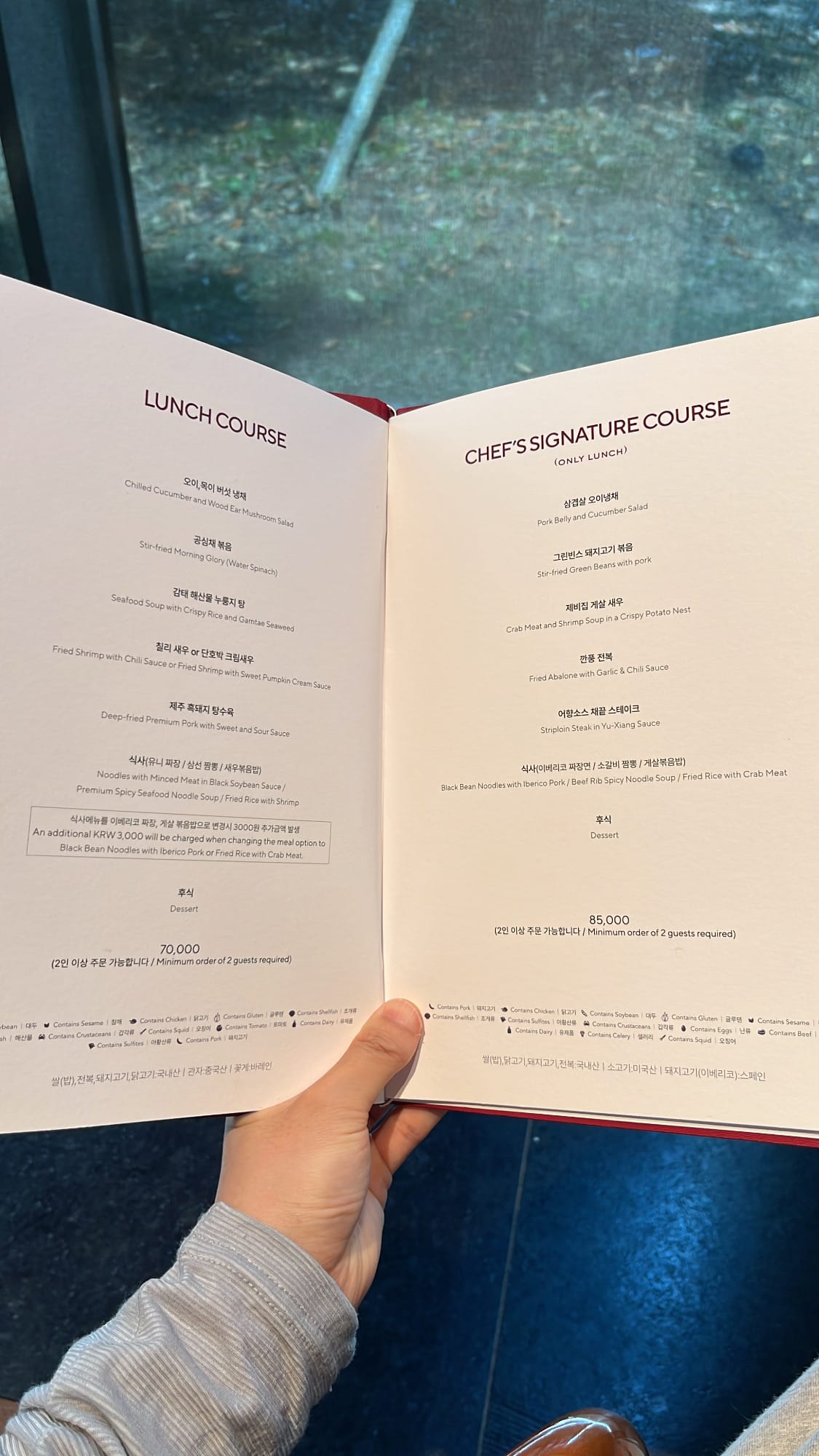 Guest holding open the red leather-bound course menu booklet inside Village de Ananti Lou Busan