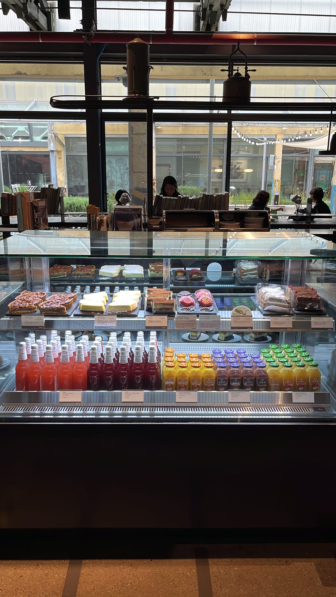 Refrigerated glass case stocked with fruit juices, cakes, and pies