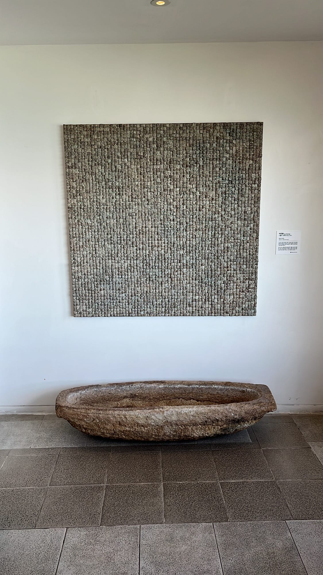 Textured square wall art piece placed above an antique stone water basin