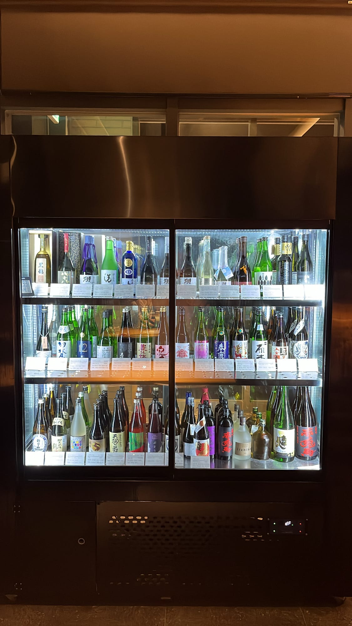 Large refrigerated glass display filled with curated craft sake at Murasaki Busan