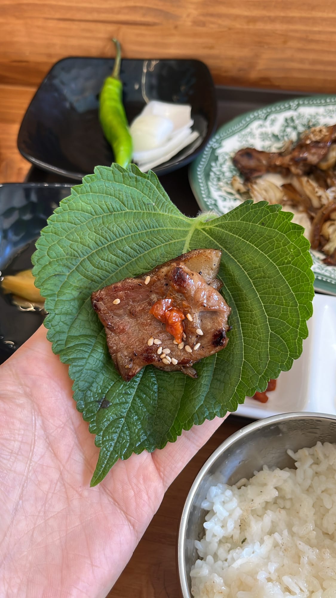 Hand holding a fresh perilla leaf wrap with grilled pork and ssamjang at Chef202 Busan